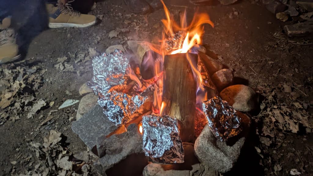 Foil-wrapped food cooking on stones in a campfire at night